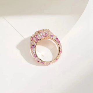 side angle view of a luxurious engagement ring featuring a large round brilliant-cut white gemstone at the center, surrounded by multiple pink and white sapphires set in a rose gold band.