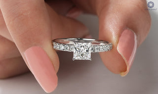 A hand holding a white gold engagement ring with a 1 carat princess cut center diamond and pavé diamond band, showcasing the sharp brilliance of the stone.
