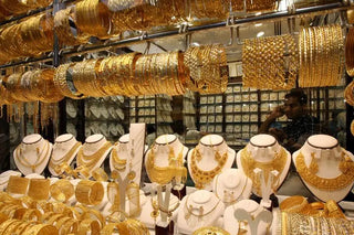 Indian shoppers browsing gold jewelry in a bustling Dubai showroom, reflecting the allure of better prices and purity.