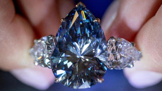 Close-up of a rare pear-cut blue diamond ring flanked by two white diamonds, reflecting brilliant flashes of blue and white light.
