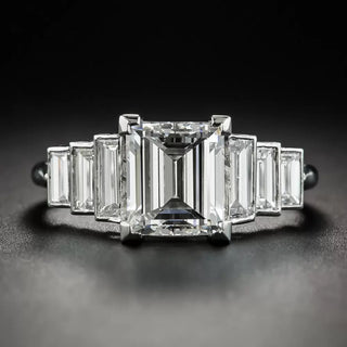 Close-up of a step-cut diamond engagement ring featuring a large rectangular center stone flanked by graduated baguette diamonds on each side, set in a sleek platinum band against a dark background.