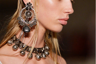 Close-up of a woman wearing a bold gemstone necklace over a sleek blazer, showcasing confidence and authority.