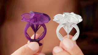 A jeweler sketching a ring design beside a wax prototype and finished piece, illustrating the design process from concept to creation.