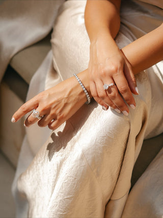 Close-up of elegant hands wearing diamond engagement rings and a tennis bracelet on champagne satin, showcasing luxury diamond jewellery