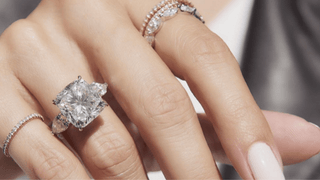 Cushion cut diamond engagement ring with pear-shaped side stones worn on a hand, paired with thin pavé bands.