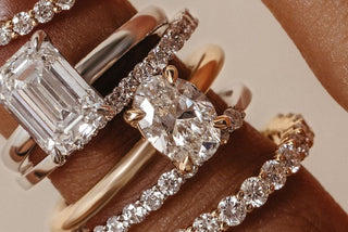 Close-up of four elegant diamond rings on a hand featuring oval, emerald, and round cut stones with pavé and solitaire settings in yellow and white gold.