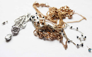 A pair of hands gently untangling delicate gold necklaces on a soft fabric surface, using a pin and patience.