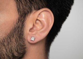 Close-up of a man’s ear with a square pavé-set diamond stud earring, highlighting short facial hair and smooth skin