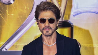  Shah Rukh Khan wearing a dark tuxedo on the red carpet, accessorized with an ornate diamond brooch pinned to his lapel, highlighting the growing trend of men wearing fine jewelry.