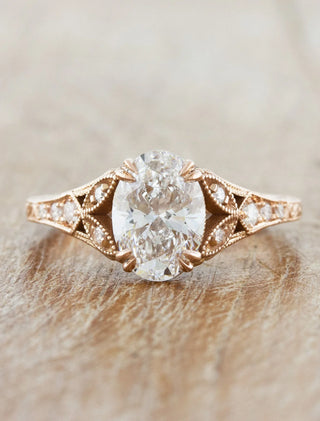 Oval diamond engagement ring set in a rose gold vintage-inspired band with intricate detailing and side diamonds.