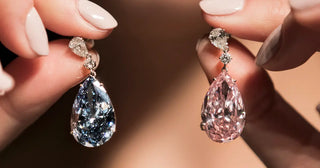 Close-up of hands holding a pair of pear-shaped gemstone earrings, one featuring a blue stone and the other a pink stone, both set with round diamond accents