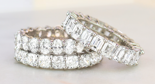 Three luxurious eternity bands featuring oval and emerald-cut diamonds set in white gold, showcasing high-clarity stones and elegant shared prong settings on a soft neutral background.
