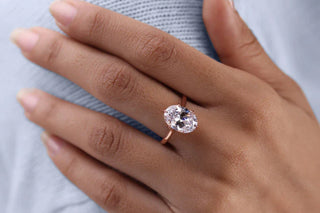 A rose gold solitaire engagement ring with a prominently visible bow-tie effect in the oval diamond, worn on the hand to demonstrate how the shadow appears face-up.