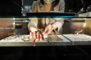 A person handing over gold jewelry to a pawnbroker across a counter, with cash and appraisal tools visible.