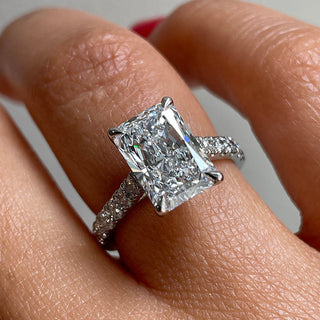 Close-up of a radiant cut diamond engagement ring with micro pavé band, set in white gold and worn on finger.