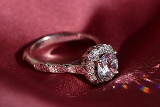 Vintage-inspired round cut diamond engagement ring with halo and pavé details, set against a deep red satin fabric.