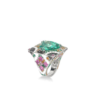 A luxurious silver statement ring featuring a large trillion-cut teal Paraiba gemstone at the center. The wide band is intricately adorned with pink, orange, green, and white gemstones in floral and geometric patterns, showcasing elaborate craftsmanship and vibrant color.