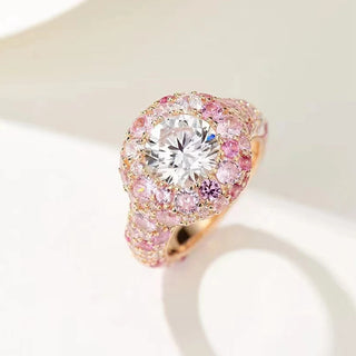 drone view of a luxurious engagement ring featuring a large round brilliant-cut white gemstone at the center, surrounded by multiple pink and white sapphires set in a rose gold band.